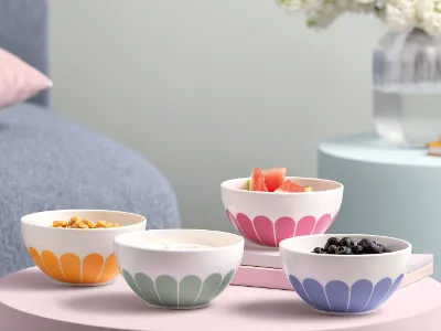 Les quatre couleurs différentes de la collection de vaisselle Fleur de Villeroy & Boch Bols Fleur de Villeroy & Boch avec divers aliments sur des tables aux couleurs pastel, accompagnés de livres et d’un vase avec des fleurs.