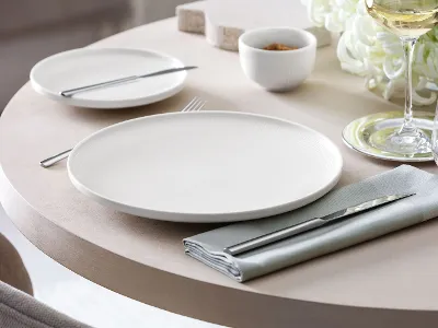 Afina dinner plate with textured relief on a laid table Close-up of an Afina dinner plate with a subtle textured relief on a laid table.