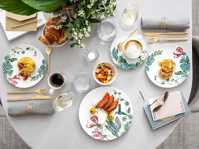 Une table de petit déjeuner Avarua Table dressée pour un repas avec des assiettes fleuries, des aliments, des boissons, des serviettes et un petit bouquet de fleurs pour décorer la table.