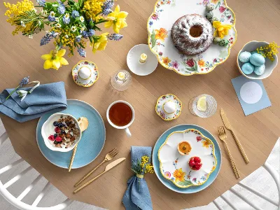 Spring Awakening, Crafted Blueberry Geschirr für einen Brunch eingedeckt Ein frühlingshaft gedeckter Tisch mit Spring Awakening und Crafted Geschirr, einem Gugelhupf, einer Schüssel Haferflocken mit Beeren, einer Tasse Tee und dekorativen Eiern.