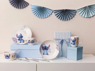 Ein Platzdeckchen-Set mit Geschirr, Tassen und Schalen zum Thema "Stitch" Ein Platzdeckchen-Set mit Geschirr, Tassen und Schalen zum Thema "Stitch" auf blauen Boxen, mit gestreifter Geschenkbox und Dekoration.