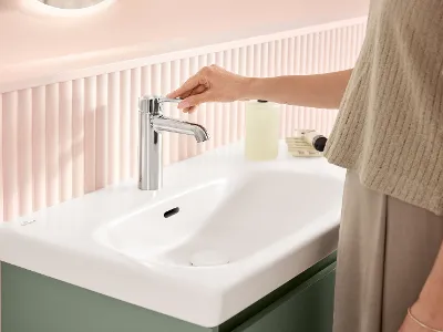 Perfekt abgestimmte und funktionale Armaturen der Skyla Badkollektion von Villeroy & Boch Eine Frau steht vor dem weißen Waschbecken und bedient die Waschbecken-Armatur in der Farbe Chrom - beide Produkte aus der Skyla Badkollektion von Villeroy & Boch.