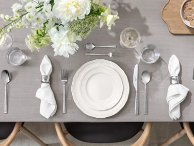 The table is set with white plates, napkins, cutlery, glasses, and a floral arrangement on a grey tablecloth.