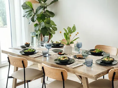 Lave Vert table with like glass and decor A wooden dining table for four with crockery and a plant centerpiece.
