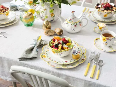 Spring Awakening Geschirr auf Ostertisch mit Fruchtsalat Ein farbenfroher Osterbrunch-Tisch, gedeckt mit floralem Spring Awakening Geschirr und einer Schüssel voller Früchte.