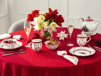 Runder Tisch mit einer roten Tischdecke für die Teestunde, mit festlichem Porzellan, Gebäck, Blumen und Weihnachtsdekorationen.