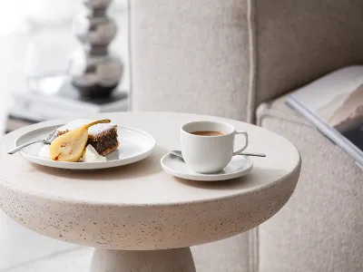 Une tasse et une assiette Afina avec du gâteau et du café Une tasse à café et une assiette avec du gâteau sur une table d’appoint moderne et avec de la vaisselle Afina de Villeroy & Boch.