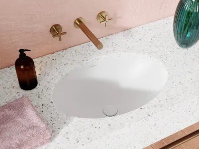 Loop & Friends Waschbecken in modernem Badezimmer Modernes Waschbecken mit Terrazzo-Arbeitsplatte, Messinghahn und Seifenspender. Ein rosa Handtuch liegt daneben, und in der Ecke steht eine Vase mit grünem Glas.