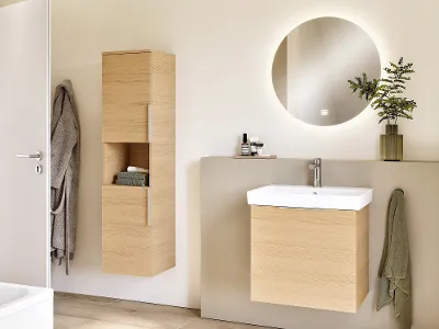 Architectura Armatur auf einem weißen Waschtisch mit Holzmöbel Modernes Badezimmer mit hellen Holzmöbeln, einem wandmontierten Waschbecken und einem runden, von hinten beleuchteten Spiegel. Minimalistisches Dekor mit einer kleinen Pflanze auf der Ablage.
