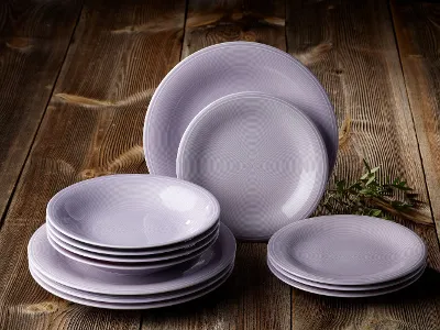 color loop plates in stone on wood table A stack of light grey plates arranged on wood with a small green plant nearby