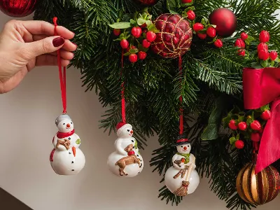 Nostalgic Ornaments Des ornements de bonhomme de neige sont accrochés à la main à un sapin de Noël décoré de rubans rouges, de baies et de boules.