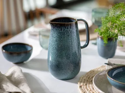 Un pot Lave bleu en céramique est posé sur une table décorée. Un pot Lave bleu en céramique est posé sur une table décorée avec de la vaisselle assortie, une petite plante verte et un set de table tissé.
