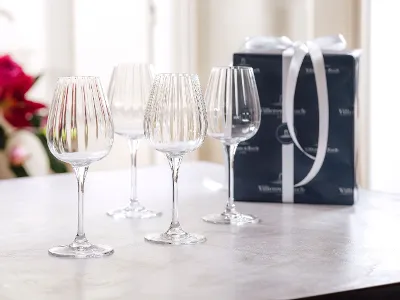 Quatre verres à vin en cristal sur une table à côté d'une boîte cadeau emballée avec un ruban blanc.
