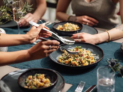 Four people enjoy a meal at one table. Lave bowls with mixed salad are placed on a blue tablecloth. 