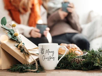 A Villeroy & Boch Statement cup on a table with a gift box A Villeroy & Boch Statement cup on a table decorated with a gift box, sprigs of fir and pastries. In the background, two people wearing jumpers are holding cups.