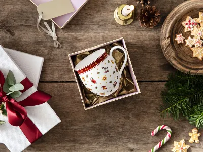 A Toy’s Delight mug in a gift box, surrounded by a white wrapped gift with a red bow, cookies on a wooden plate.