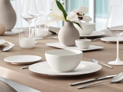 Elegant table decoration with white crockery, glasses and cutlery on a wooden table. Elegant table decoration with white crockery, glasses and cutlery on a wooden table. A vase with white flowers serves as a centrepiece.