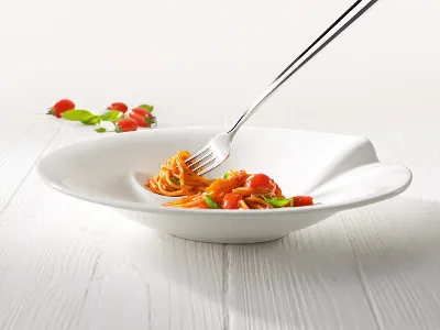Pasta Passion Spaghettiteller mit Gabel und Nudeln Eine Gabel in einer weißen Villeroy & Boch Pasta Passion-Schüssel hält eine kleine Portion Spaghetti mit Kirschtomaten und Basilikum auf einem hellen Holztisch.