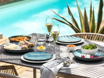 Al Fresco Poolside Table Setting A beautifully set outdoor dining table with plates, glasses of champagne, bread, and fresh salads beside a swimming pool.
