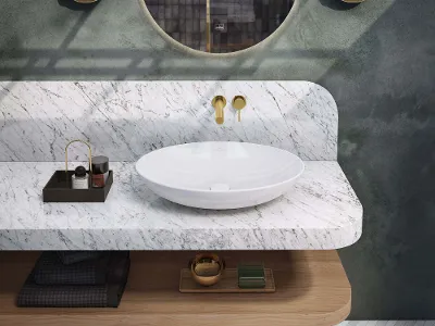 Lavabo Loop & Friends bianco su piano in marmo bianco Bagno moderno con lavabo Loop & Friends bianco, piano in marmo bianco, specchio rotondo More to See e accessori eleganti su un pavimento a spina di pesce.