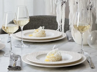 Elegant table setting with two Manufacture plates Elegant table setting with two Manufacture plates of dessert, wine glasses, and white decor on a marble surface.