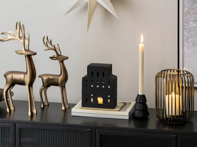 Two metal reindeer, candle holders Two metal reindeer, candle holders and a black, house-shaped lantern on a black sideboard.