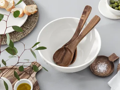 Utensili Artesano in una ciotola bianca Utensili Artesano in una ciotola bianca, più una piccola ciotola di legno con sale, un tagliere con olio d'oliva, un piatto con pane, una ciotola con olive e rami di eucalipto su una superficie chiara di Villeroy & Boch.