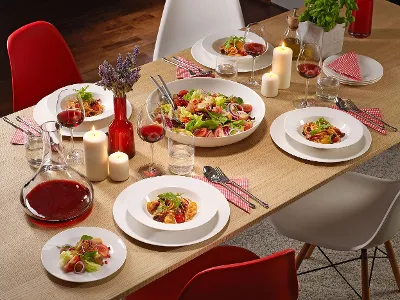 Ein Esstisch mit For me Tellern voller Salat, Pasta, Gläsern Rotwein, Kerzen und einer Karaffe mit Rotwein.