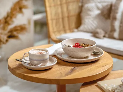 Perlemor Tasse mit Kaffee neben Schüssel Eine Perlemor Tasse mit Kaffee und eine Schüssel mit Müsli auf einem Holztisch.