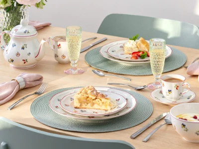 A set table for two with dessert plates, teacups, a teapot, champagne glasses, and floral-patterned porcelain from Petite Fleur.