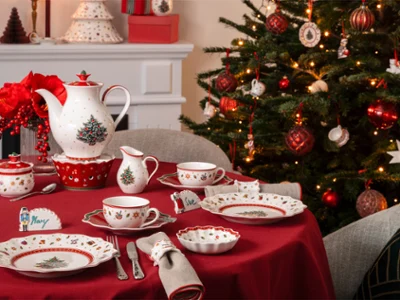 A table set with crockery and cutlery A table set with crockery and cutlery featuring Christmas motifs, next to a decorated Christmas tree and an illuminated mantelpiece.