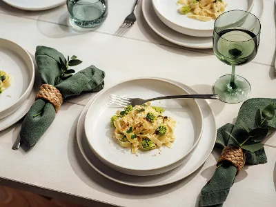 aus-craftedcotton-indoor-food-nopeople-flatplateset8651 Crafted Cotton Flat Plate complimented with green linen napkin, silverware, Like green glassware ontop of a white wooden table.