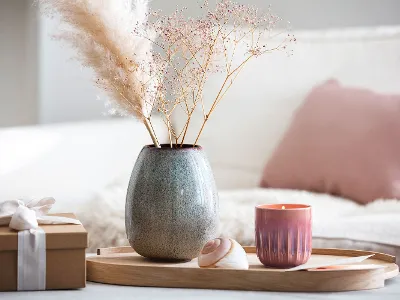Holztablett auf dem eine Lave Vase und eine Perlemor Kerze mit getrockneten Blumen stehen, neben einem verpackten Geschenk.