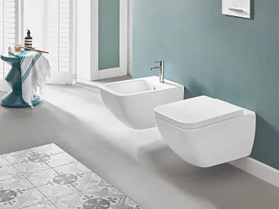 Weißes Venticello Wand WC mit Bidet und Regal Das moderne Bad mit blaugrünen Wänden verfügt über ein Venticello-Wand-WC und ein Bidet. Ebenfalls ein Regal mit Toilettenartikeln und einem gerahmten Foto sowie einen kleinen Beistelltisch mit Handtuch und Badeutensilien neben den Fensterläden.