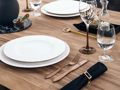A bronze cutlery set lies next to a white plate on a wooden table.