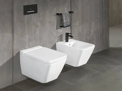 Weiße Toilette und Bidet aus der Kollektion Finion Ein modernes Badezimmer mit einer weißen wandmontierten Finion-Toilette und einem weißen Bidet. Über der Toilette befindet sich eine schwarze Spülplatte und über dem Bidet ein schwarzer Handtuchhalter mit einem grauen Handtuch an einer grau gefliesten Wand.