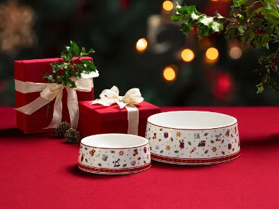 Due ciotole Toy's Delight per animali con motivi natalizi Due ciotole Toy's Delight per animali con motivi natalizi su un tessuto rosso, accanto a due scatole regalo rosse con nastri bianchi e decorazioni verdi.