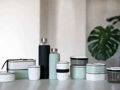 Verschiedene Lunchboxen aus der Kollektion To Go und To Stay Ein Set Mehrwegbehälter und -flaschen „To go und To stay“ von Villeroy & Boch in unterschiedlichen Größen und Farben, arrangiert auf einem Tisch, im Hintergrund eine Topfpflanze.