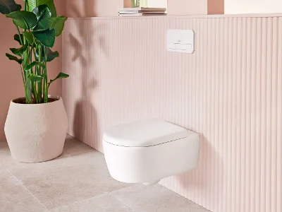 Le WC suspendu de la collection de salle de bain Skyla de Villeroy & Boch Le WC suspendu de la collection de salle de bain Skyla de Villeroy & Boch dans la couleur Stone White (blanc mat), y compris une plaque de commande ViConnect blanche, est présenté dans une salle de bain élégamment meublée dans des tons pastel et à côté d'une plante d'intérieur.