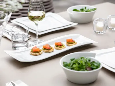 A table set for a meal with plates of appetizers, glasses of white wine, a bowl of salad, and tea lights.