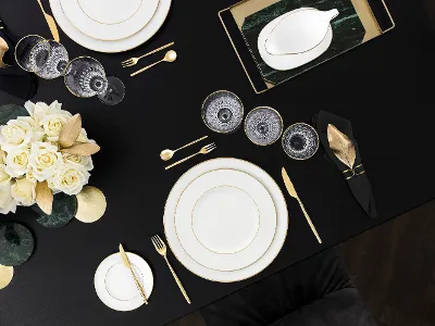 Elegantes weißes Porzellan mit goldenen Akzente Tischgedeck mit weißem Porzellangeschirr, goldenen Akzenten, modernen Bestecken und weißgelben Rosen.