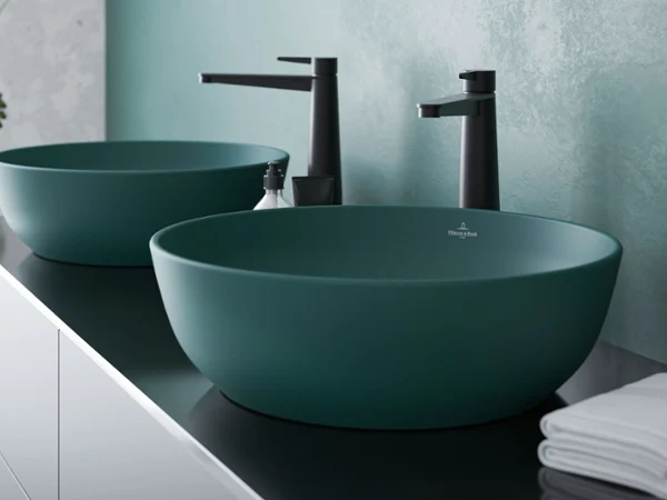 Grüne Artis Waschbecken mit schwarzer Conum Armatur Zwei grüne Waschbecken mit schwarzen Wasserhähnen auf einem schwarzen Unterschrank, daneben ein ordentlich gefaltetes weißes Handtuch.
