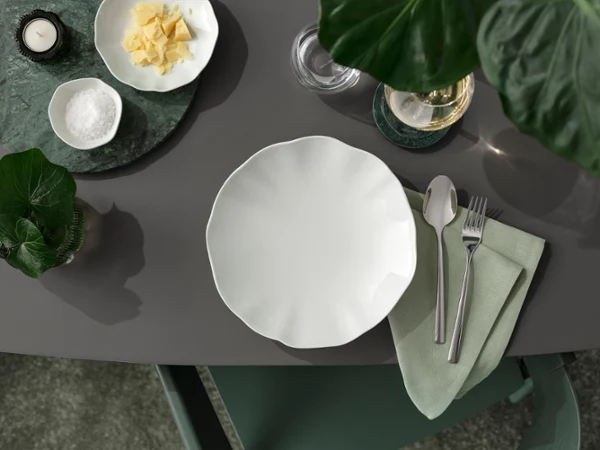 Ein ordentlich gedeckter Esstisch mit einem weißen Teller der Kollektion Pura Ein ordentlich gedeckter Esstisch mit einem weißen Teller der Kollektion Pura, Besteck auf einer Serviette und kleinen Schüsseln mit Lebensmitteln von oben gesehen.