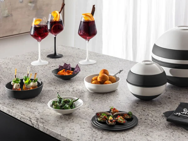 Elegant cocktail party spread with La Boule and Manufacture Rock wine glasses Elegant cocktail party spread with red wine cocktails, appetizers, croquettes, salad, and black-and-white serving bowls on a counter.