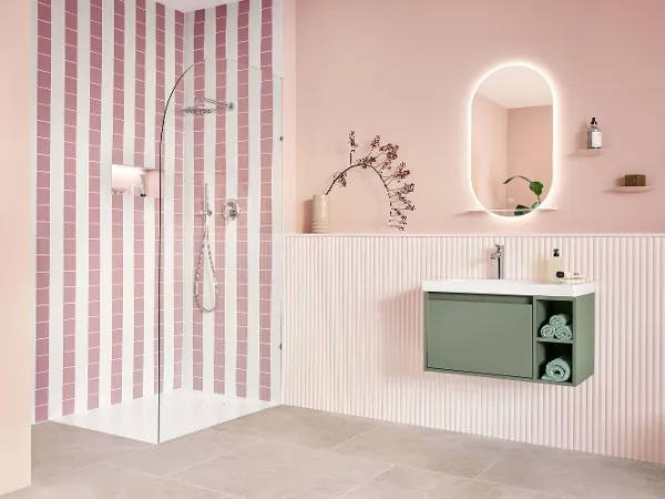 Grüner Skyla Waschbeckenunterschrank an einem Waschplatz in rosa Badezimmer Modernes Badezimmer mit rosa-weiß gestreifter Dusche, ovalem Spiegel, wandmontiertem Waschbecken und hellem Holzboden.