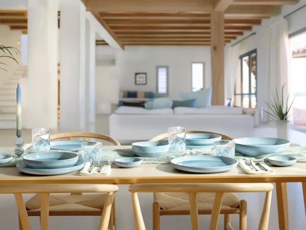A dining table set with blue Perlemor Aqua tableware and glasses in a bright, modern, open-plan living area with wooden beams.