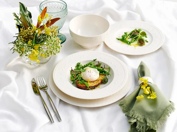Cellini Set for One, showcasing fresh ingredients on the plates, is paired with silver cutlery and complemented by a green napkin, the setting is further elevated with elegant Like glassware and a vase of florals.