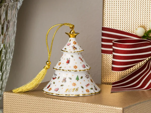 christmas classics ornament tree A porcelain Christmas bauble with gold detailing and a tassel, placed next to a wrapped present tied with a red-striped ribbon.
