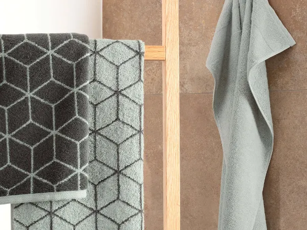 Handtücher Carré hängen auf Holzleiter Handtücher mit geometrischem Muster in Grün- und Grautönen hängen an einem Holzgestell und einem Wandhaken.