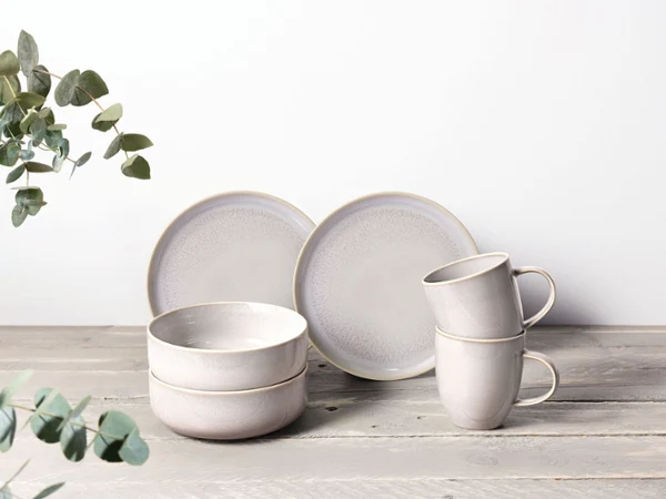 A Crafted Cotton set consisting of two plates, two bowls, and two mugs. A Crafted Cotton set consisting of two plates, two bowls, and two mugs with eucalyptus branches in the background.